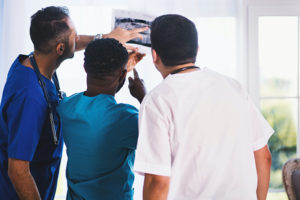 New Jersey pain management doctors in blue, green, and whit scrubs from left to right look at an x-ray