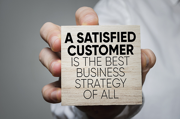 A satisfied customer is the best business strategy of all printed on a block being held out by a hand of NJ NCR company employee